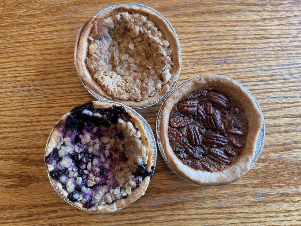 Apple, blueberry, and pecan mini pies together on a wooden table