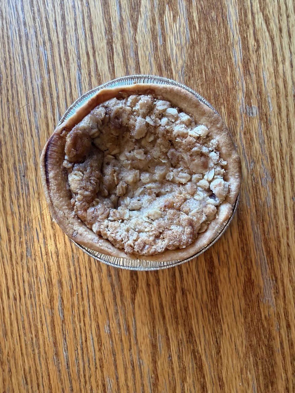 An individual apple crumble pie on a wooden table