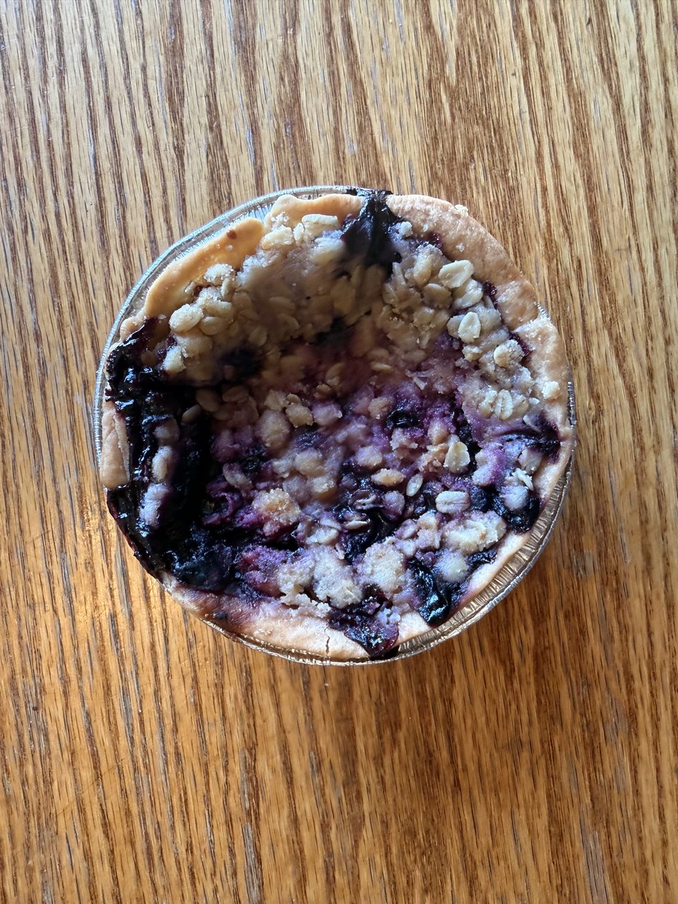 An individual blueberry crumble pie on a wooden table
