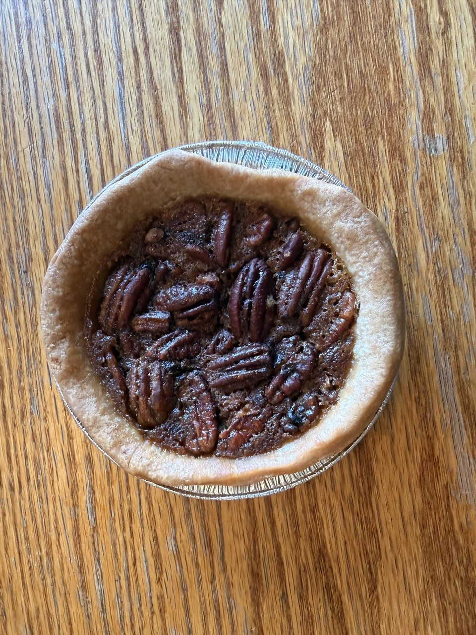 An individual pecan pie in a foil tin on a wooden table